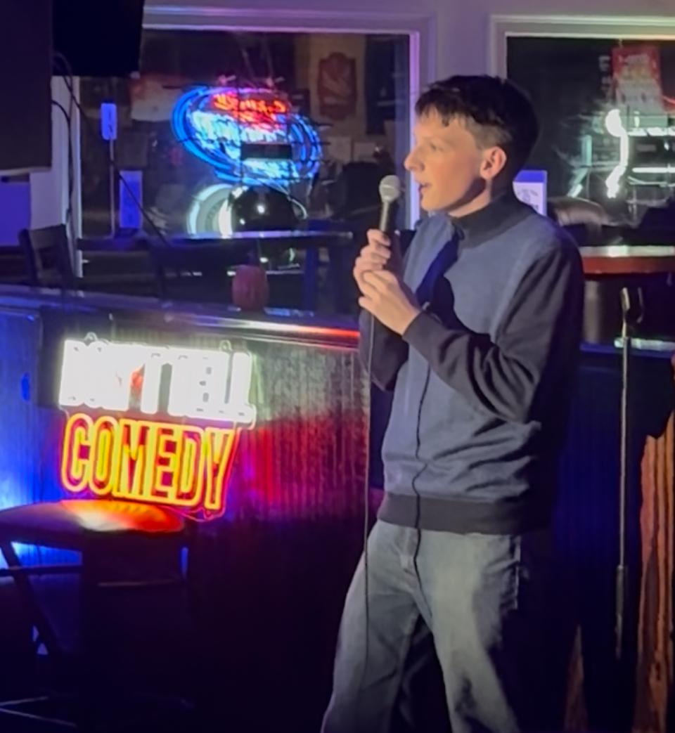 Lucas Estrella performing beside a neon comedy sign
